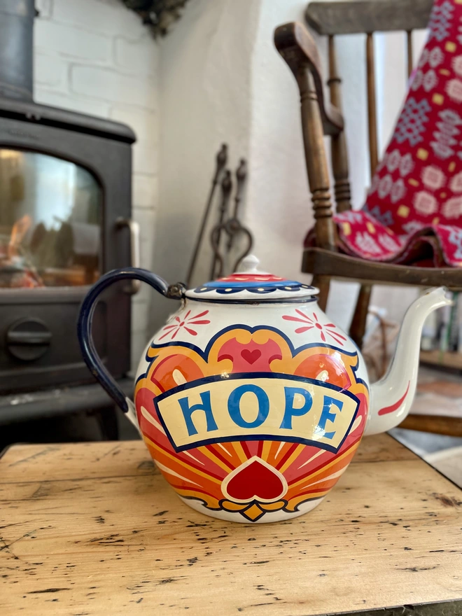 White vintage teapot, hand painted with a fairground inspired design in pink, orange, yellow and red. 'Hope' is painted in a banner across the centre.