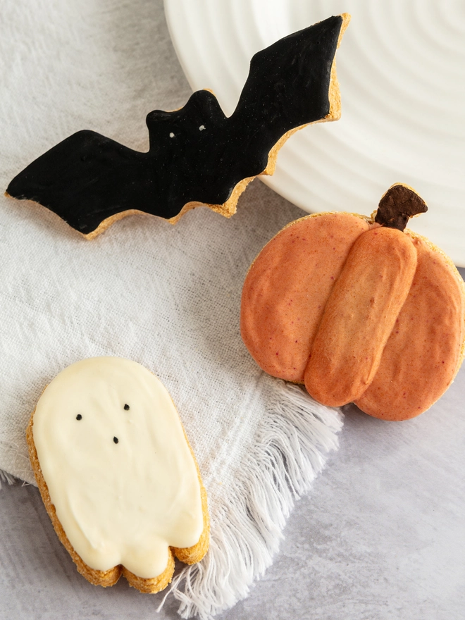 Overhead view of pumpkin, ghost and black bat iced dog biscuits arranged on a cream plate.
