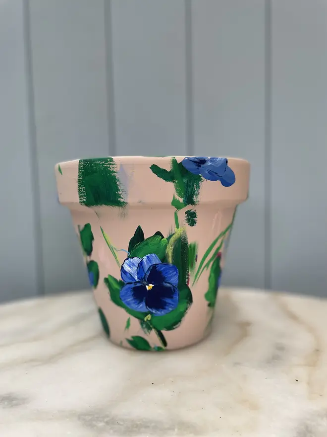 Unique hand-painted terracotta pot featuring blue pansy flowers on a dark cream background
