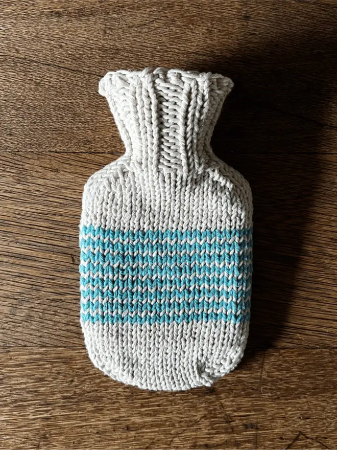 Mini Hot Water Bottle with turquoise striped knitted string cover on an oak table