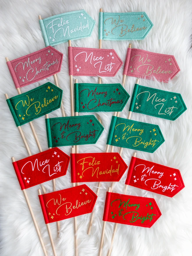 A range of christmas flags in a variety of colours and messages. The flags are made from felt and the text is written in cursive glitter letters