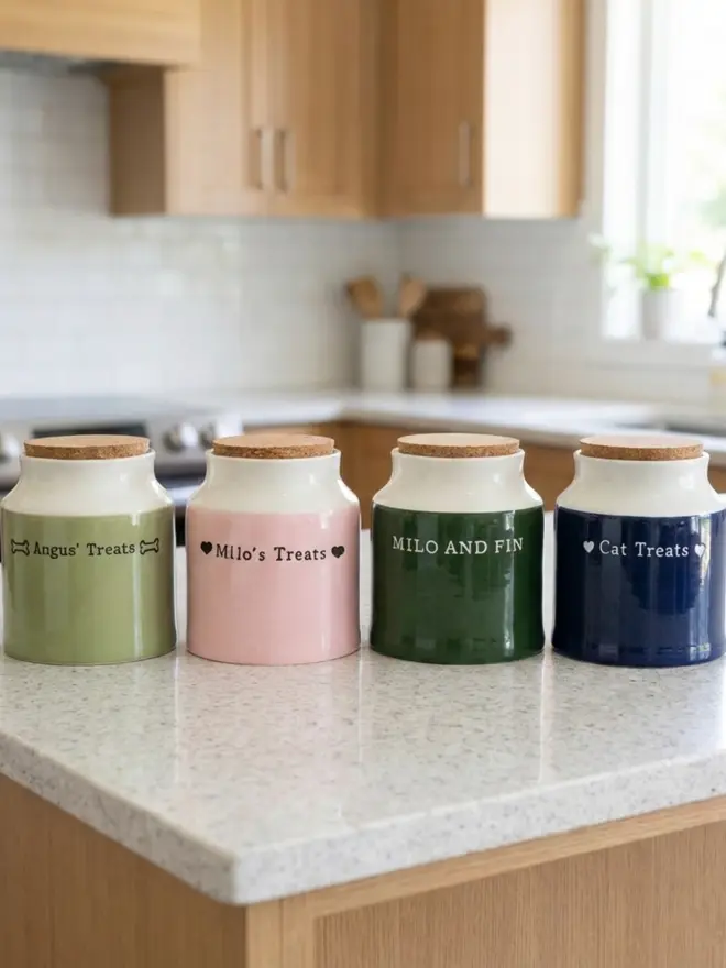 four dog treat jars lined up on a kitchen counter