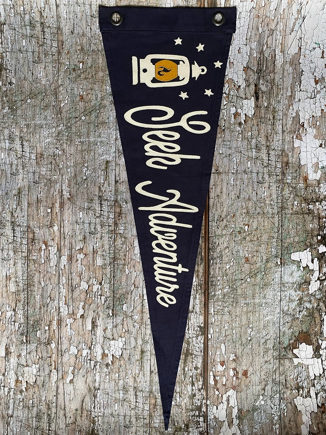 A navy canvas pennant flag hung vertically with the words 'Seek Adventure' in Ivory canvas and a hurricane lantern in ivory and mustard canvas.