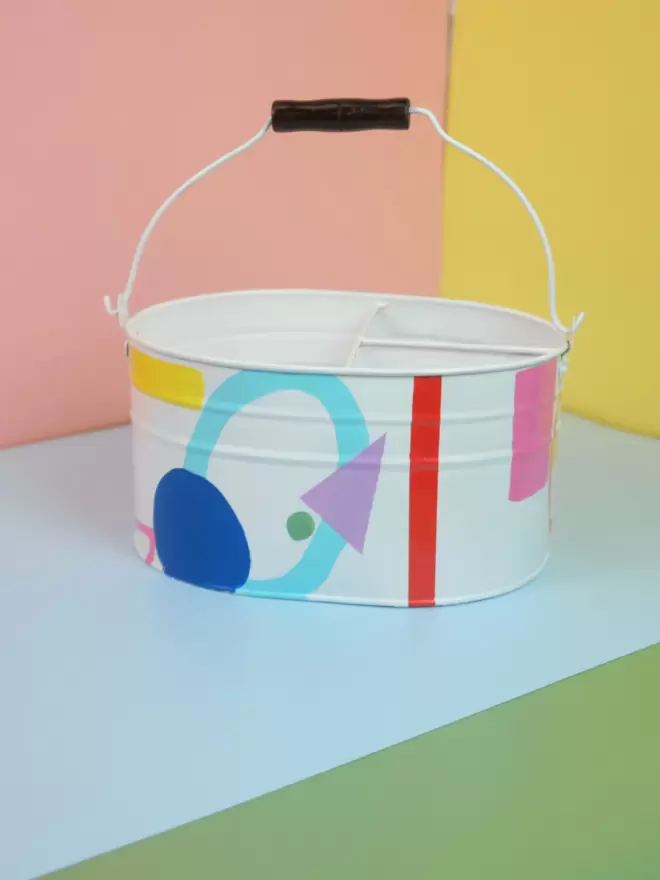 Hand painted garden storage bucket by Julie-Anne Pugh, London based artist. The base colour is white and features lots of bright coloured circles, triangles and rectangles 
