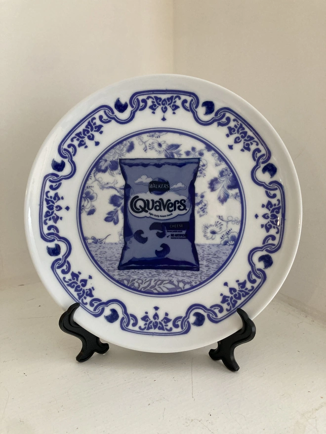 Blue and white Delft style decorative plate featuring a packet of Quavers crisps in the centre.
