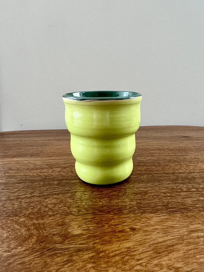 ceramic wavy tumbler with lime green glaze on the outside and dark green on the inside. the tumbler holds 250ml of liquid and sits on a wooden table