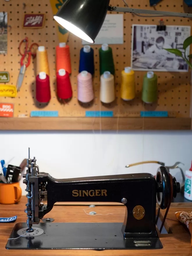 Vintage singer chain stitch machine on a desk with colourful threads behind.