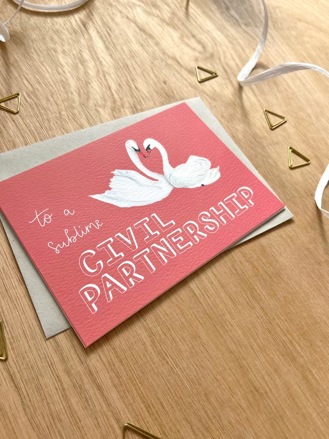 a greetings card with a deep pink background featuring two swans with their necks meeting in a heart shape, and the phrase “to a sublime CIVIL PARTNERSHIP”