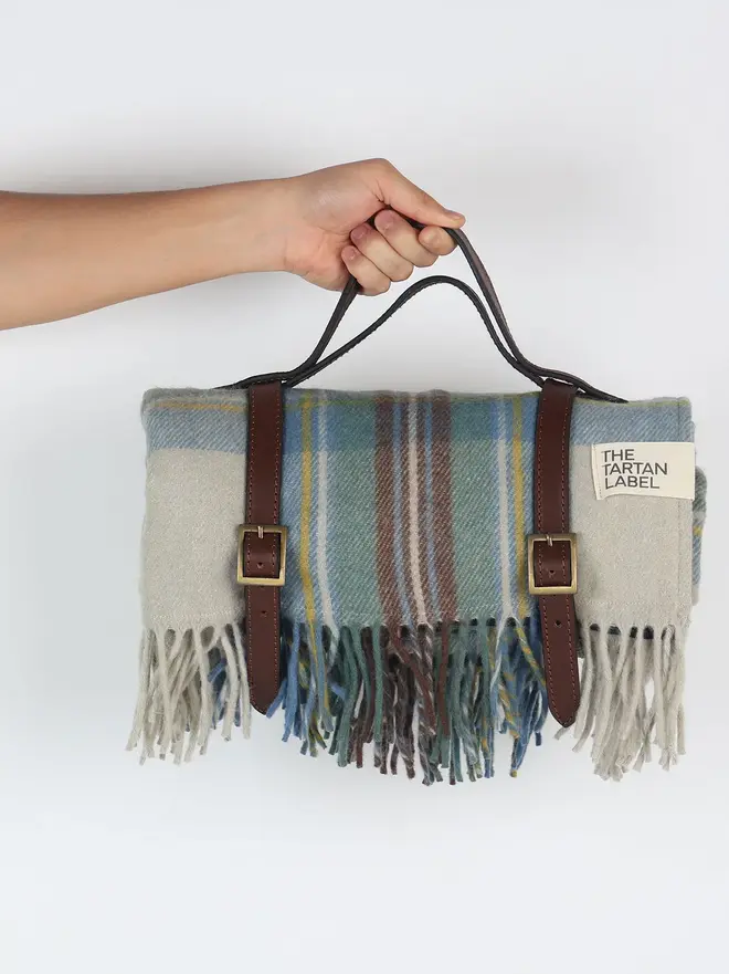 Stewart Muted Blue Picnic Blanket, a person holding a blue picnic blanket in front of a white backdrop. 