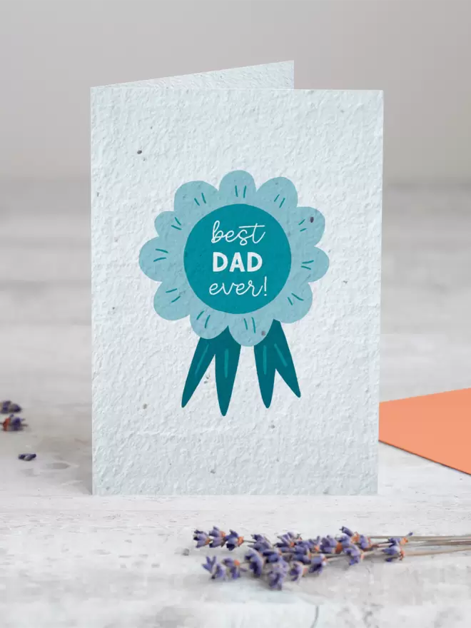 Illustration of a blue rosette with ‘Best Dad Ever’ on it with a sprig of Lavender placed in the foreground