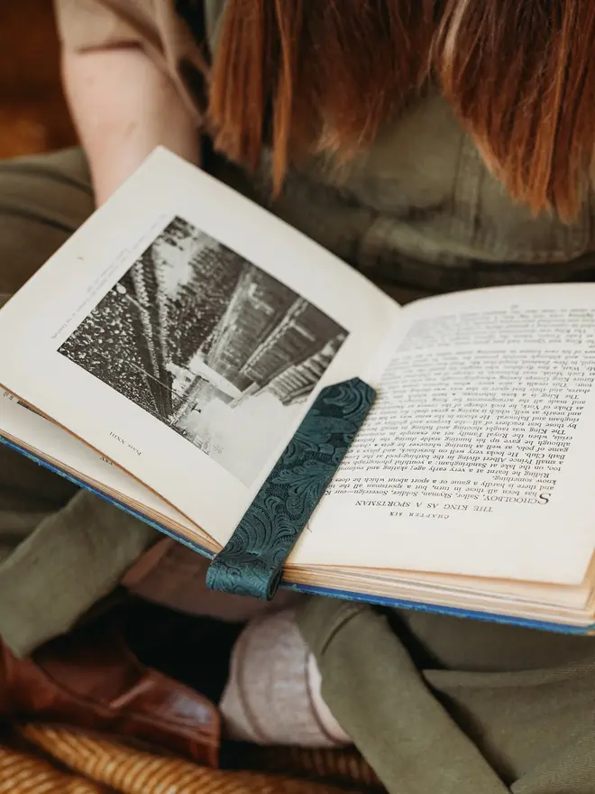 botanical leather bookmark. a dark green bookmark laid between two pages of a book.