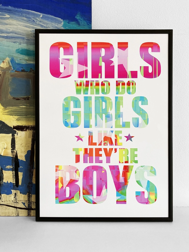 Framed multicoloured typographic print of a Blur song lyric from Girls and Boys - “Girls who do girls like they’re boys”.  The print rests against a blue and yellow abstract painting.