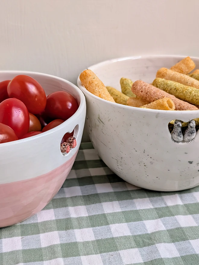 pigeon and robin bird couple bowls in pink or splattered grey design with crisps snacks and tomatoes on a green gingham table cloth
