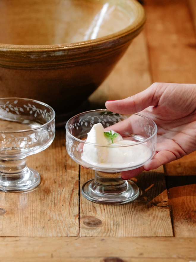 Two clear glass dessert bowls with an etched leaf pattern filled with ice cream and set on a rustic wooden table.