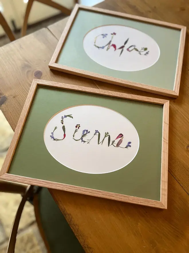 Personalised Original Pressed Flower Name In Frame, a pair of framed flower name prints sitting  on a wooden surface. 