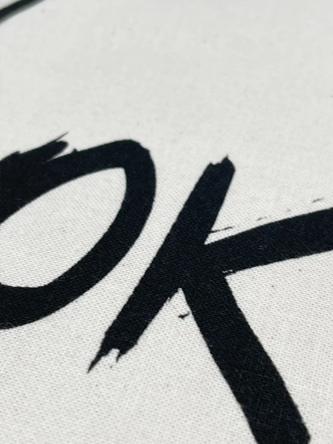 Close up of the OK of the OK tote bag, black ink drawn line on natural cotton.