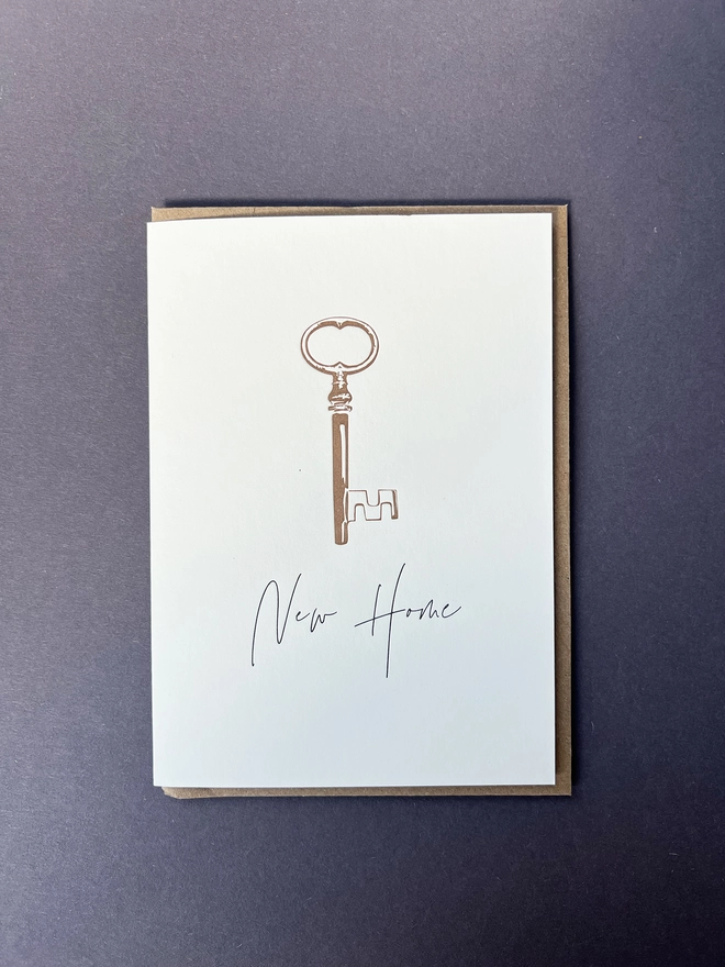 A metallic bronze vintage key with “New Home” beautifully written in a modern calligraphy underneath. 