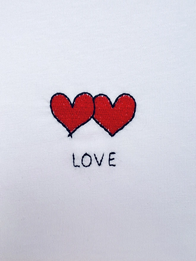     White T-shirt embroidered with two red hearts and the word “Love”