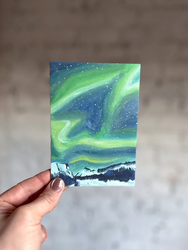 a greetings card featuring an illustration of the northern lights above a snowy landscape