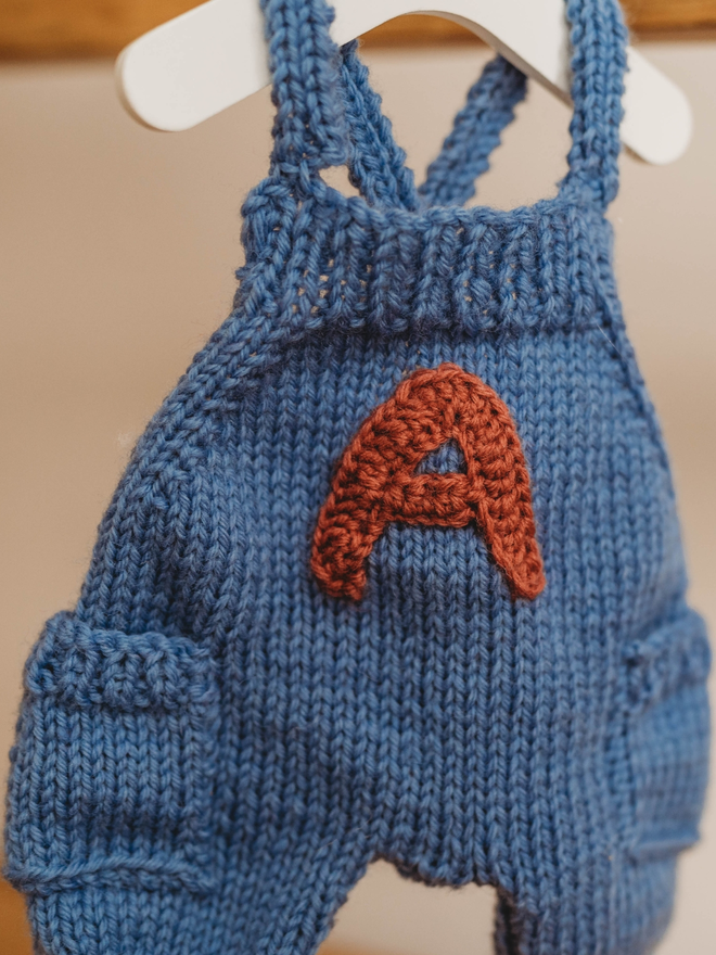 hand knitted personalised blue teddy bear dungarees on toy hanger close up