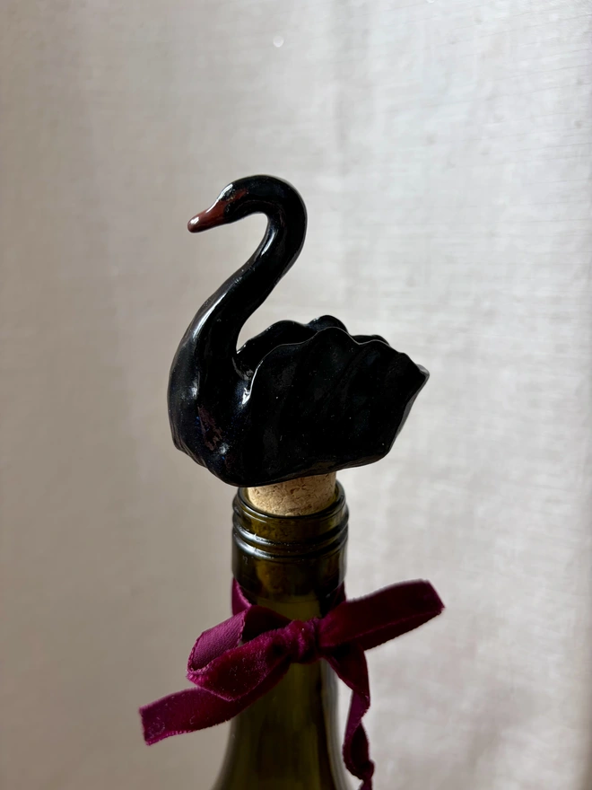 A black ceramic, swan shaped bottle stopper, in a bottle of wine