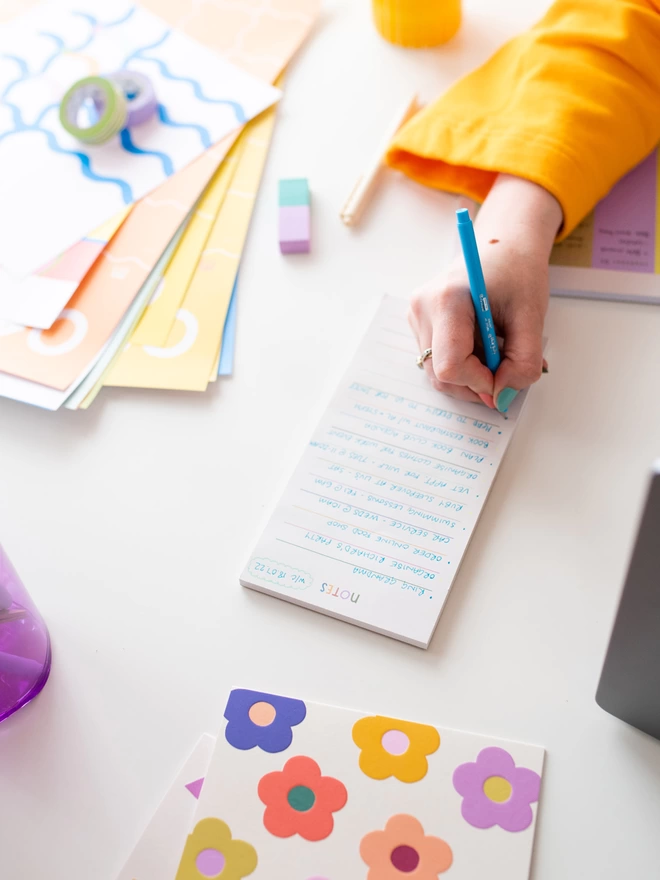 Woman in orange jumper writes on rainbow coloured line notepad