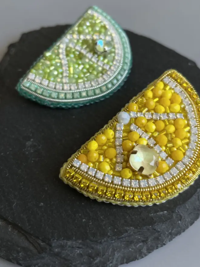 Lemon and lime slice beaded brooch, placed on  a black slate in the shape of a heart. 