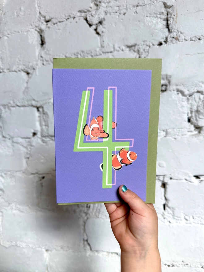 a purple card with a big green number 4 and two clown fish illustrations and a green envelope