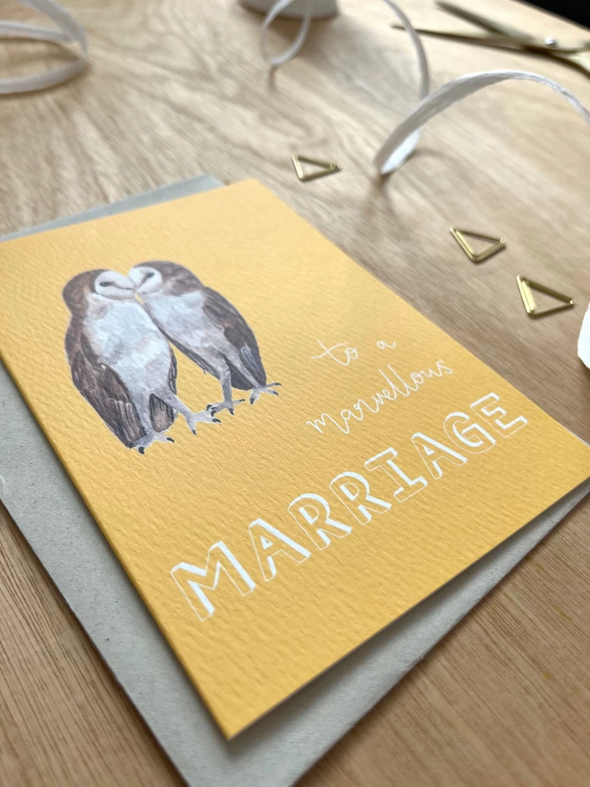 a greetings card with a bright yellow background featuring two kissing barn owls and the phrase ‘to a marvellous MARRIAGE”