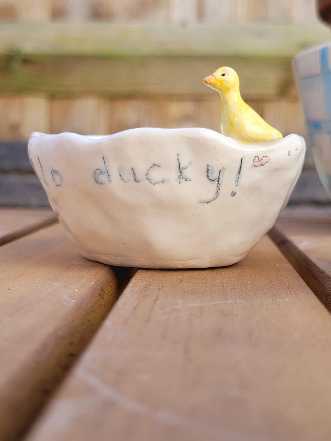 a small ceramic pot on a wooden table with the words hello ducky on the side and a yellow ceramic modelled duck on the edge 