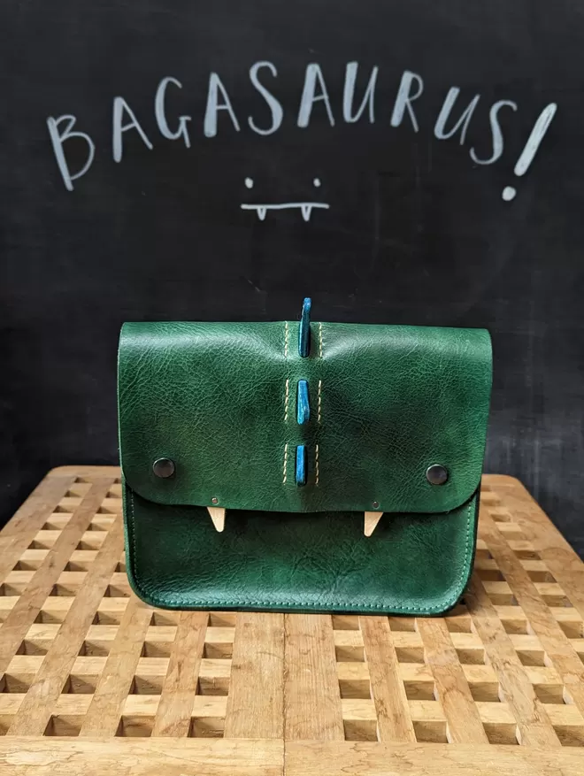 Front view of green leather 'Bagasaurus' backpack with turquoise spikes and pointed white fangs