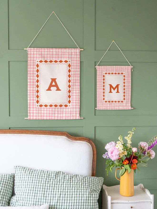 Personalised Gingham Initial Fabric Banner, in pink and red hanging on a green wall. 