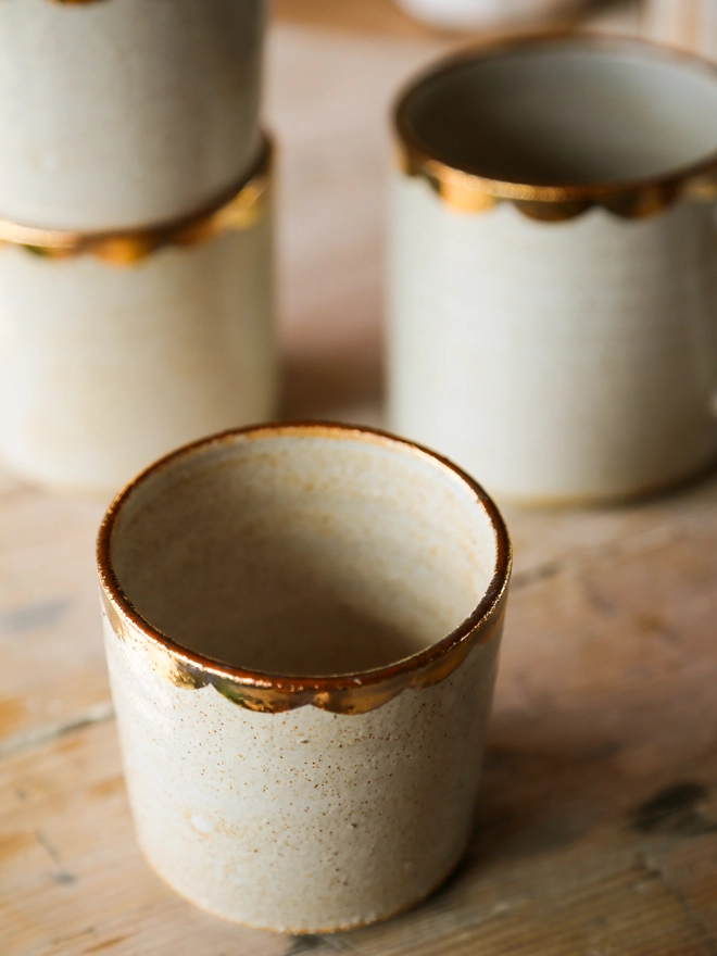 white stoneware drinking beaker with gold scallop decoration around the rim