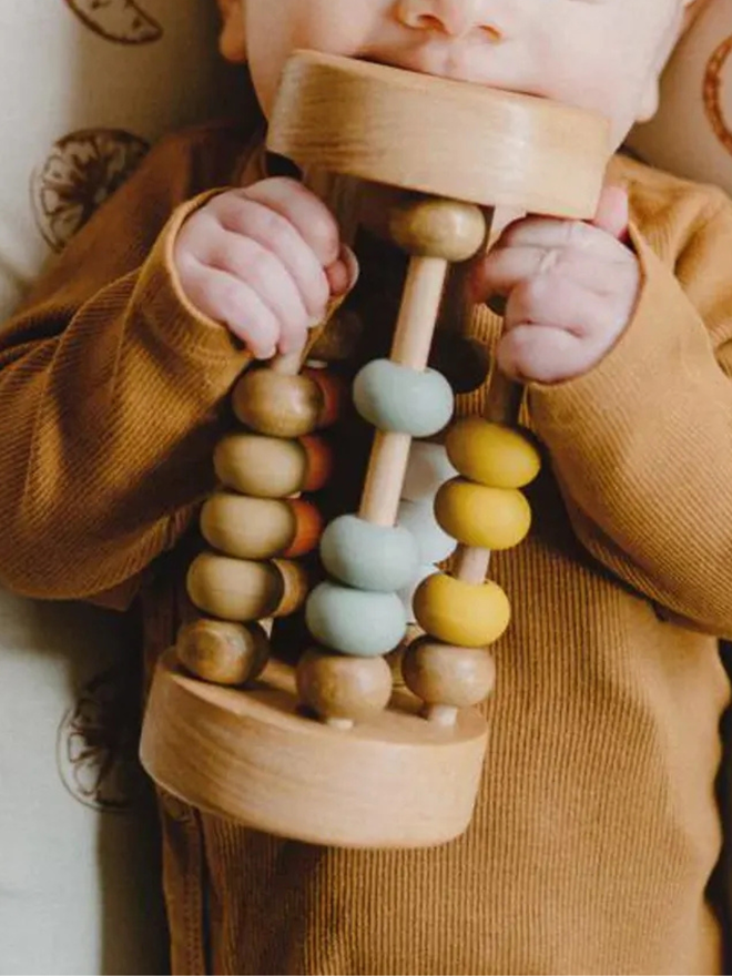 rolling wooden abacus rattle toy. a round wooden rattle toy with silicone and wooden abacus beads, being played with by a baby.