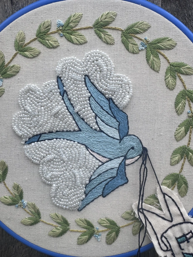 Close up of one of the hoops containing a blue bird in front of a white beaded clouds 