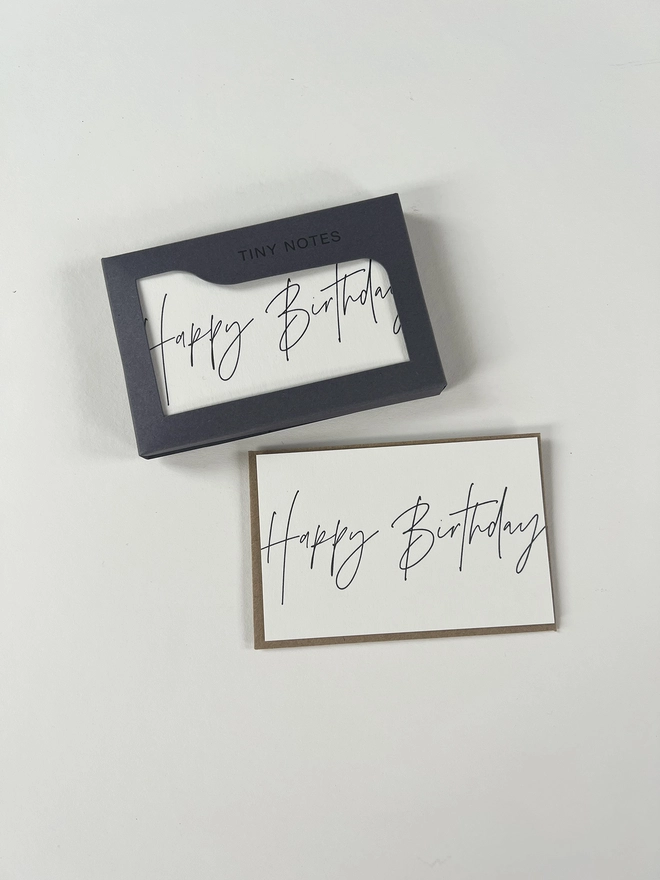 Letterpress happy birthday notes in their letterpress box, image shows one card out of the box with it's Kraft brown recycled envelope. Happy birthday is written in a modern calligraphy style.