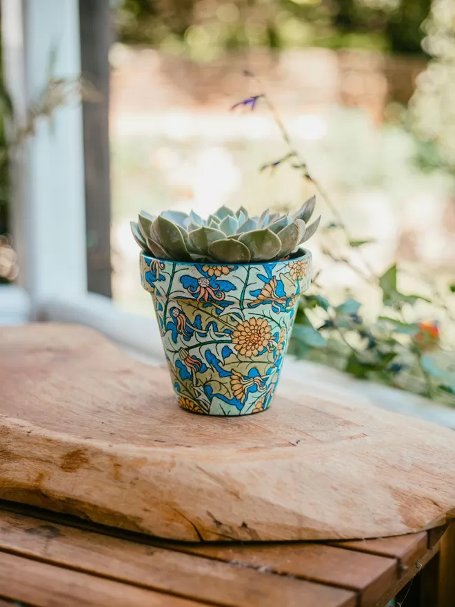 Art Nouveau Dandelion Design Plant Pot seen on a wooden board outside.