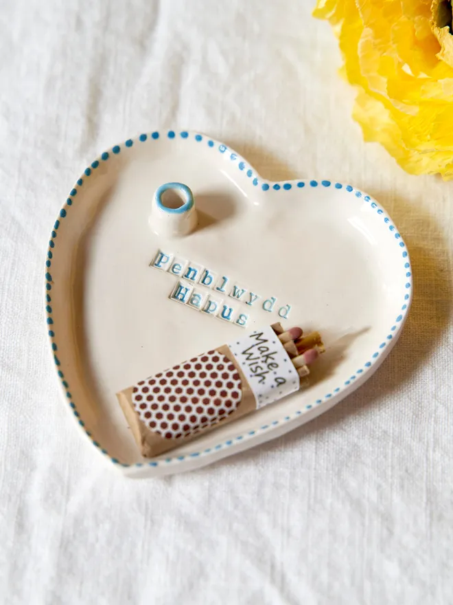 Handmade ceramic heart dish stamped with "Happy Birthday" featuring a blue dotted rim on a plain white table cloth 