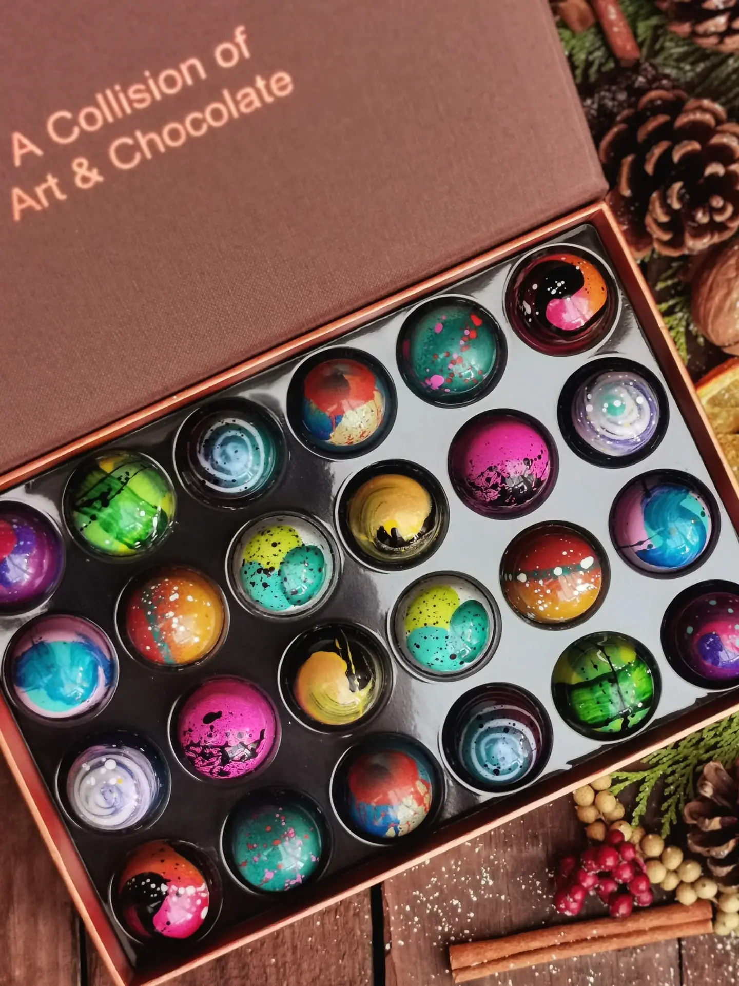 box of 24 beautifully decorated, colourful chocolates, on a background with pine cones and oranges