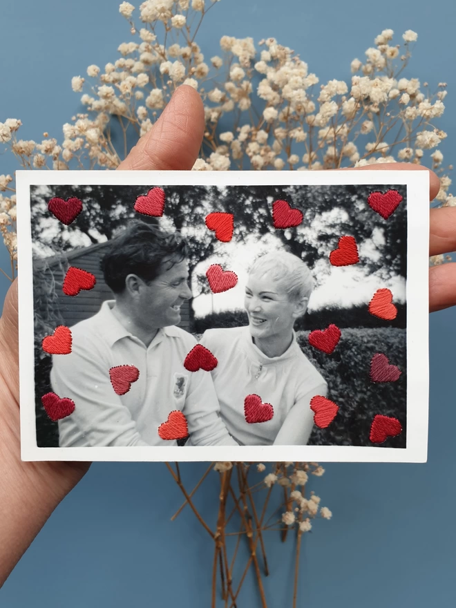 B&W couple photo, with shades of red hand embroidered hearts held against blue background