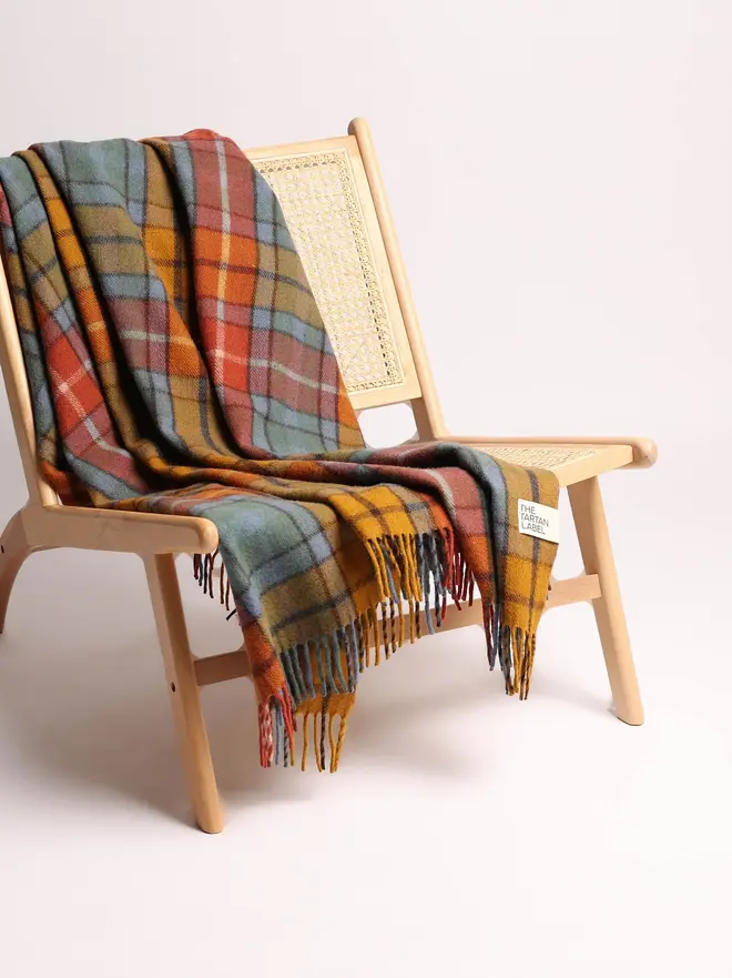 Buchanan Antique Blanket, a colourful blanket draped over a wooden chair on a white surface against a plain backdrop. 