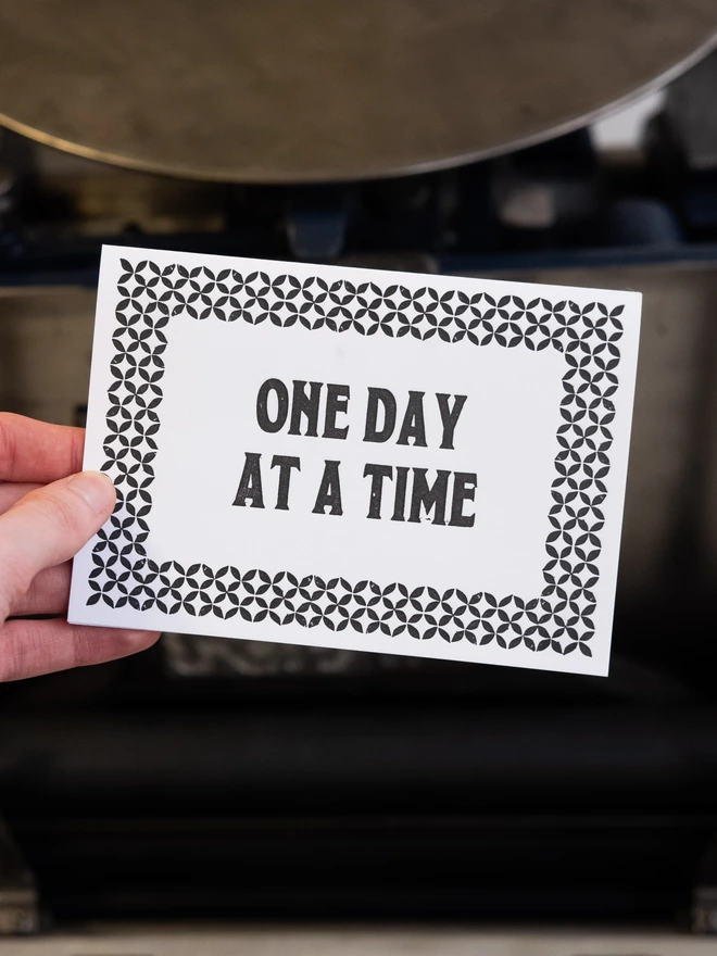 Letterpress card with text design. "One day at a time," surrounded by art-deco styled border