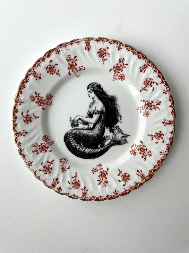 a vintage plate with a really ornate border in the centre is printed a vintage illustration of a mermaid