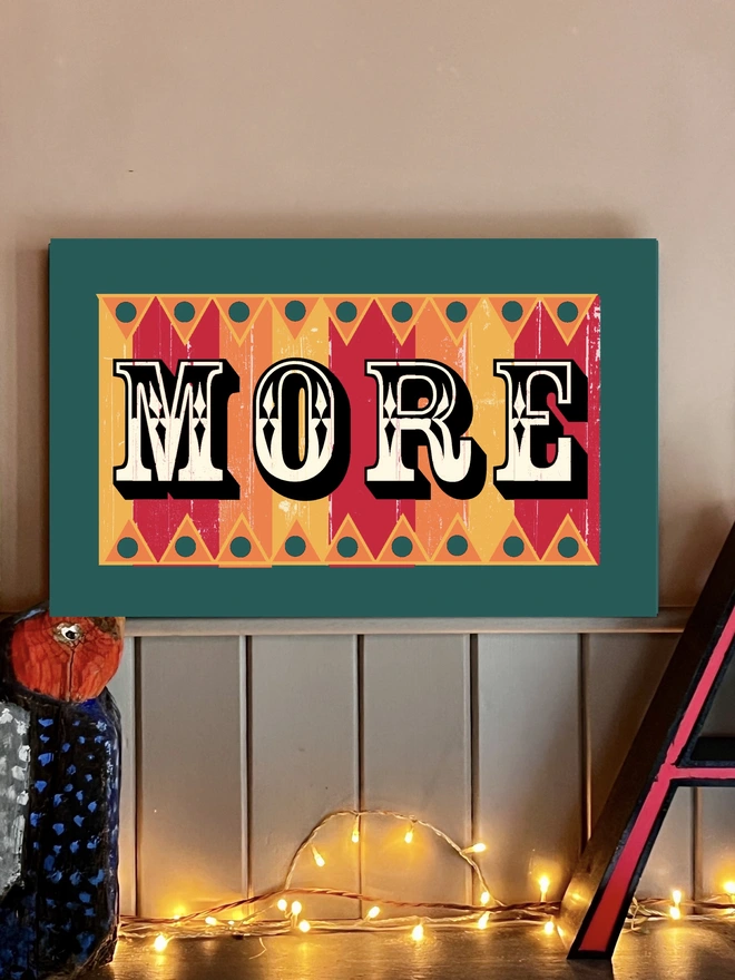 colourful MORE sign made from reclaimed wood with a teal frame, hand painted fairground lettering and with orange pink and yellow stripes, with orange and yellow zig zag patterns  top and bottom