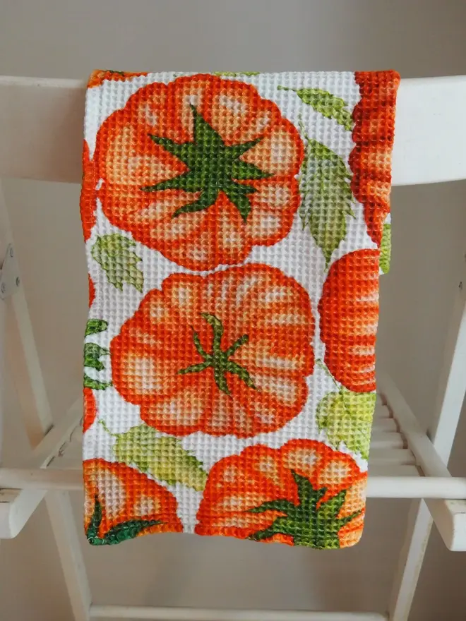 Tomato Waffle Tea towel, folded on a white chair. 