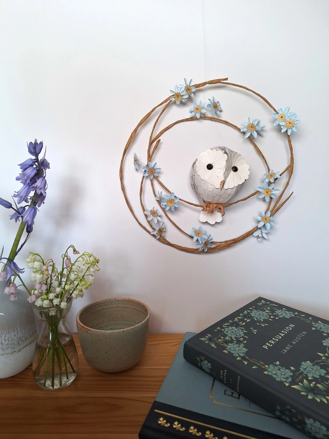 Handmade sculpture of a baby barn owl perched on a wreath of blue tree blossom flowers