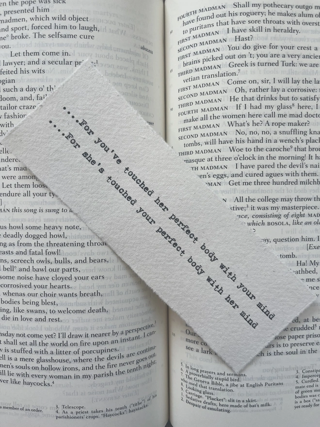 A handmade cotton rag paper bookmark with deckled edges, featuring a custom quote typed in black ink with a vintage antique typewriter.