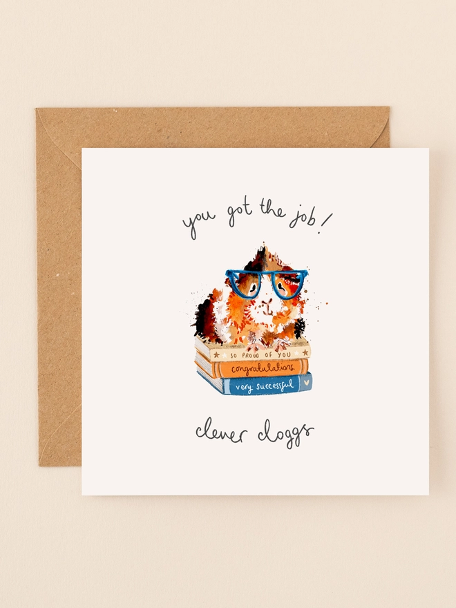 A whimsical illustration of a guinea pig wearing oversized glasses, perched atop a stack of books titled "Success Stories." The guinea pig gazes confidently ahead, embodying a sense of accomplishment. Above the scene, the playful, handwritten message "You got the job! Clever Clogs" adds a touch of humor and warmth. The design combines soft colors and charming details, making it a delightful way to congratulate someone on their new job.