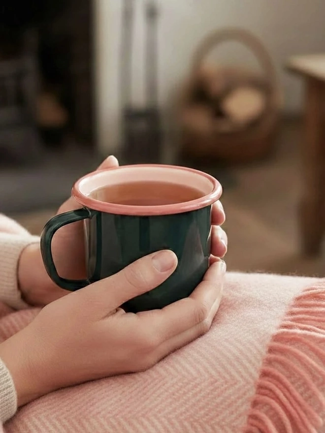 Enamel Mug, an enamel mug held by a person above a pink blanket on a sofa. 