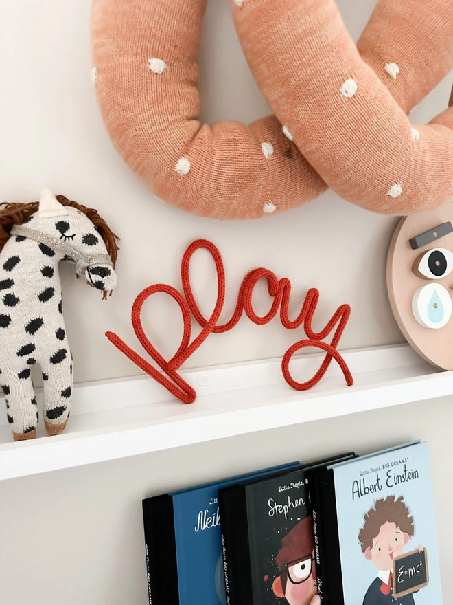 A shelf with a 'play' wire word sign on display next to some kids accessories and decorations in a child's bedroom or a nursery setting. 